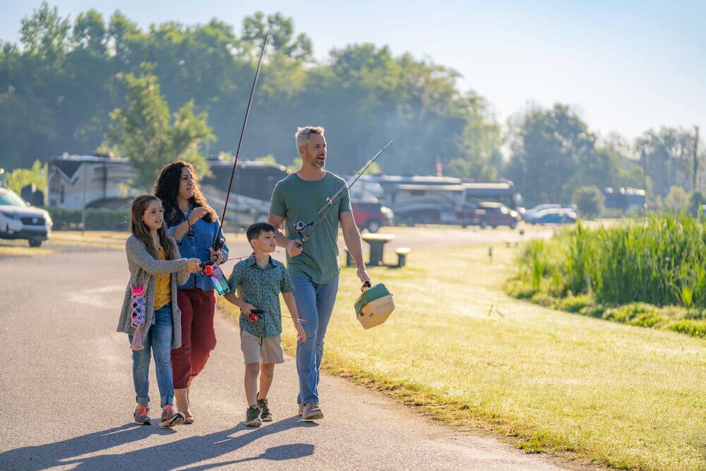 A family walking with fishing gear at toward the lake at CreekFire RV Resort in Georgia.