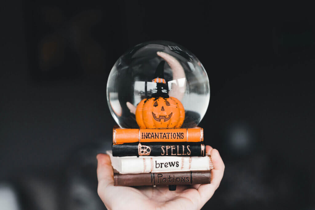 Jack-o'-lantern inside of a snowglobe that is set on books that say, "Incantations, Spells, Brews, and Potions"