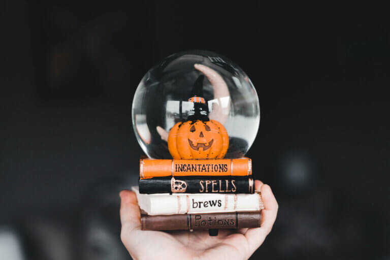 Jack-o'-lantern inside of a snowglobe that is set on books that say, "Incantations, Spells, Brews, and Potions"