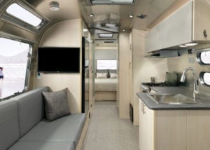Inside of an RV with a couch, sink, TV, and bedroom