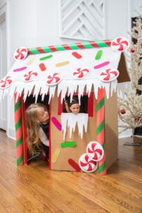 Life-sized gingerbread house with Christmas decorations on the outside and a child peering through the door