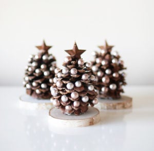 Three pinecone Christmas trees decorates with white bulbs and a brown star