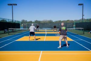 Blue and yellow tennis court with four people playing